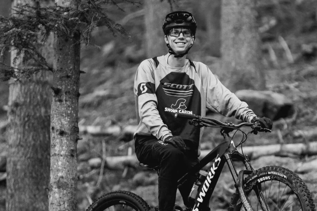 Vététiste portant un équipement Shore-Carbon, souriant tout en roulant sur un sentier forestier